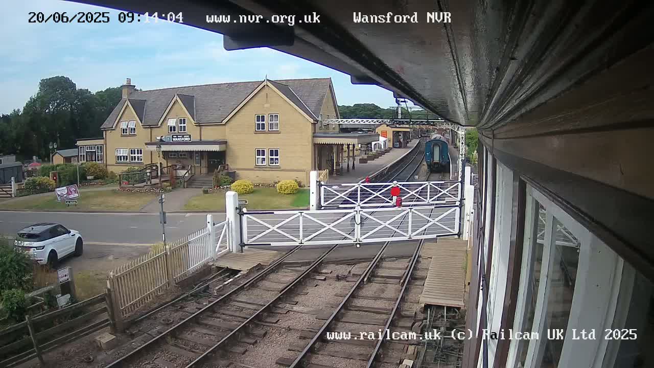 A train is approaching a railway crossing near a two-story building on a partly cloudy day.