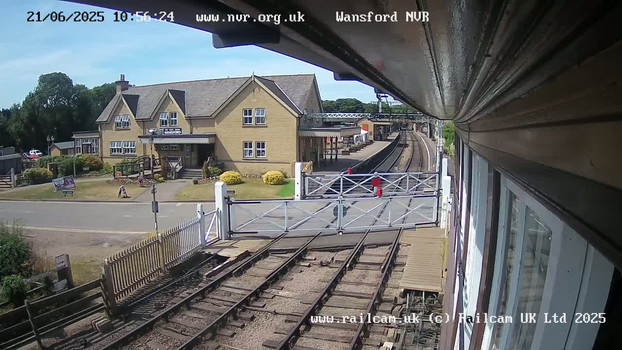 A sunny day at a train station with a two-story building, railroad tracks, and a level crossing gate.