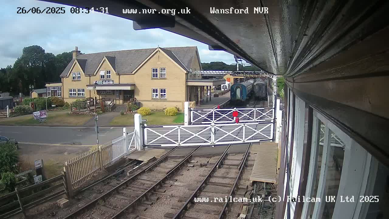 A train sits at a station platform next to a building under partly cloudy skies.