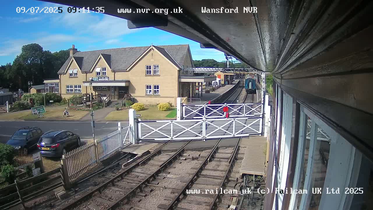 A train is arriving at a small, light-colored train station on a sunny day.