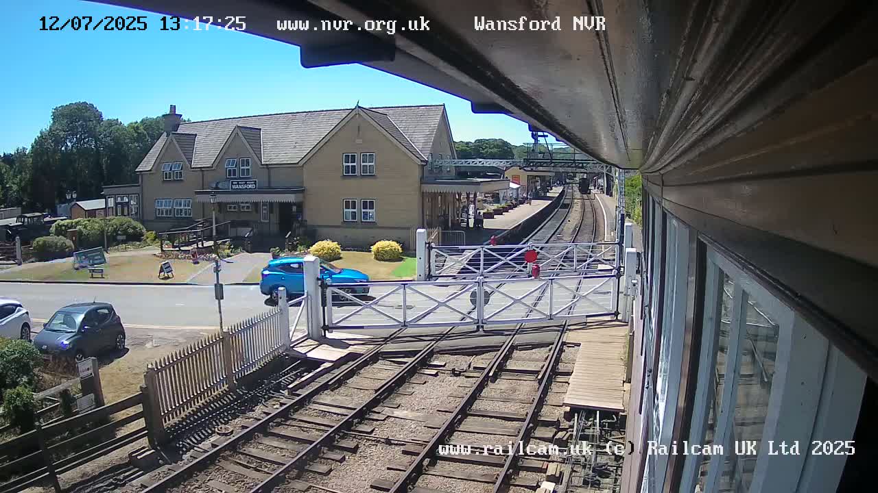 A train is arriving at a small, light-colored train station on a sunny day.
