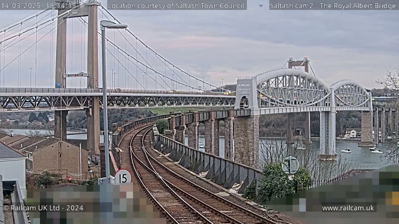 A railway track leads toward two bridges spanning a waterway under an overcast sky.