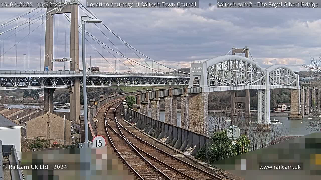 Under a cloudy sky, a railway line curves towards two bridges spanning a body of water.