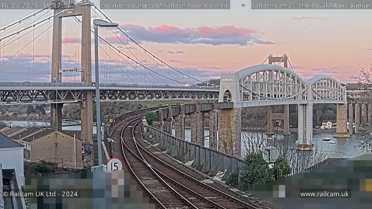 Two bridges span a river at sunset, with train tracks in the foreground.