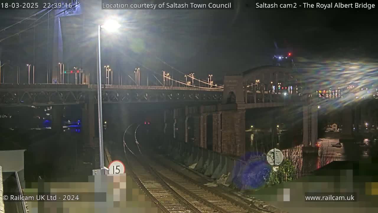 A nighttime view of a train track leading toward a suspension bridge under a clear, dark sky.