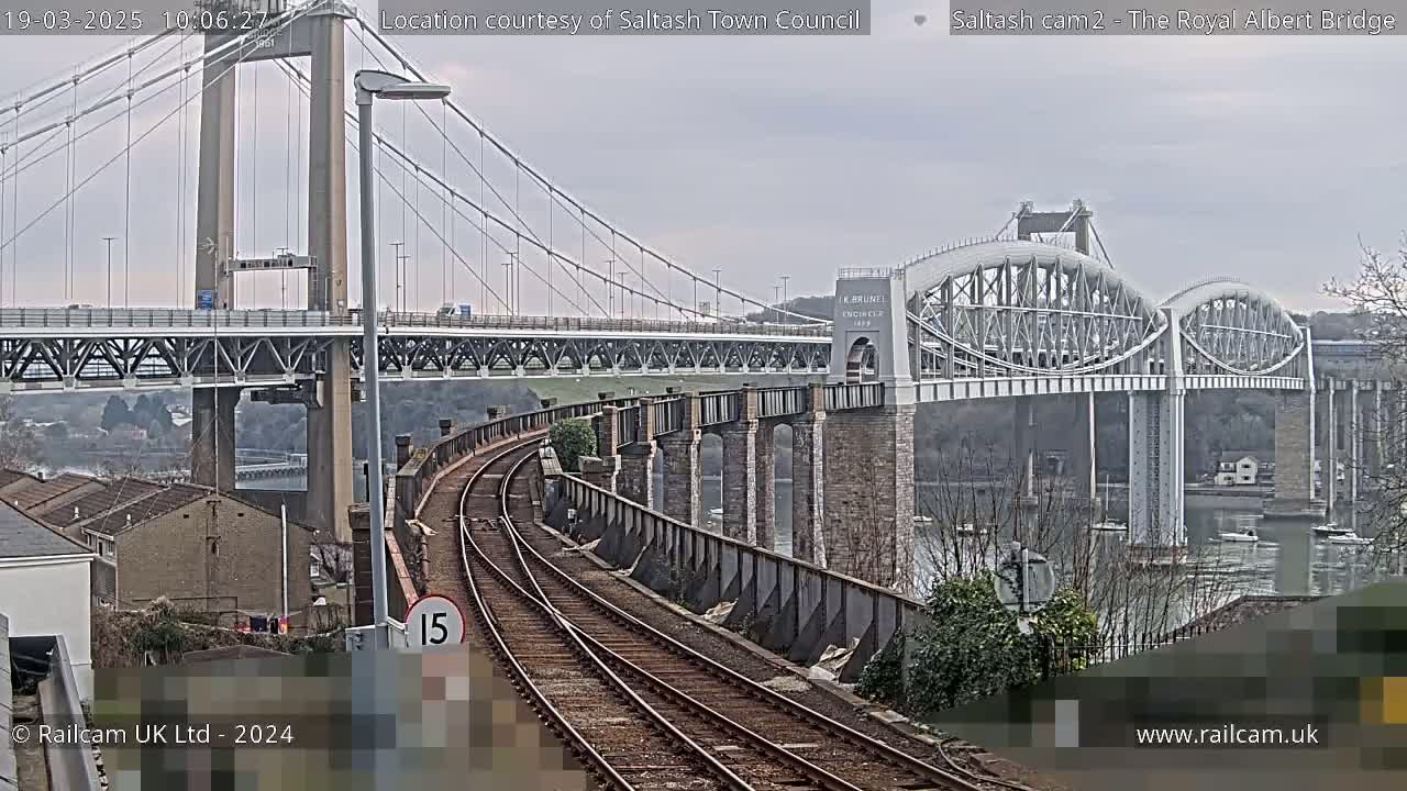 Train tracks curve toward two bridges over a body of water under an overcast sky.