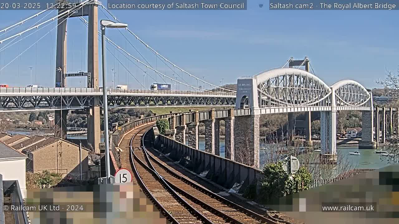 Two bridges span a waterway under a sunny sky, with train tracks curving toward one of the bridges in the foreground.