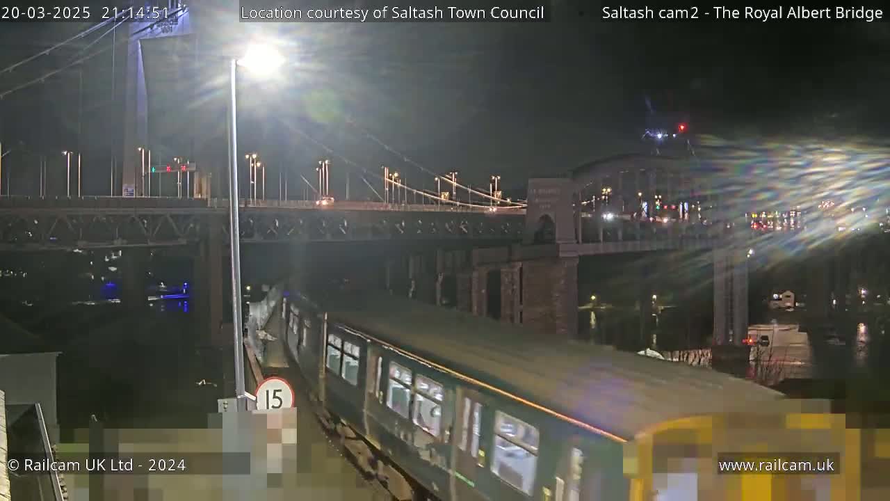 At night, a train passes under a bridge with cars driving on it.