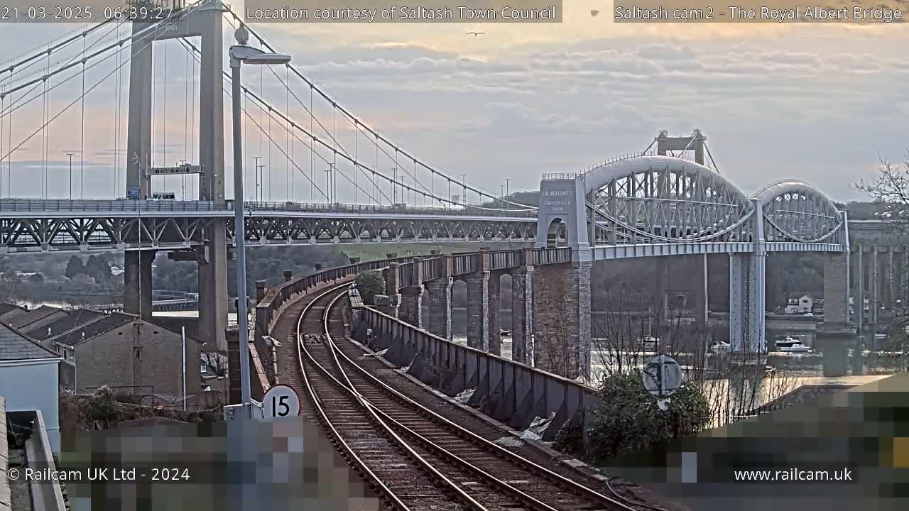 A railway track curves toward two bridges spanning a body of water under an overcast sky.