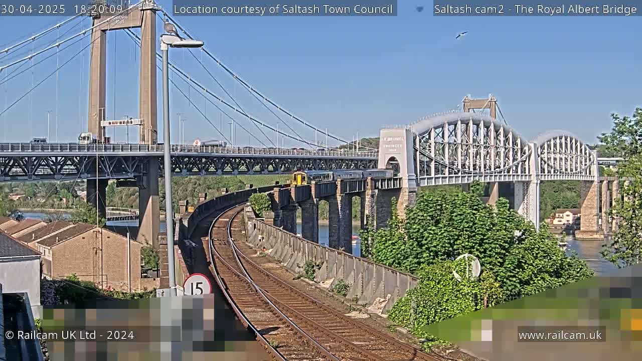 A train crosses a railway bridge under a suspension bridge on a sunny day.