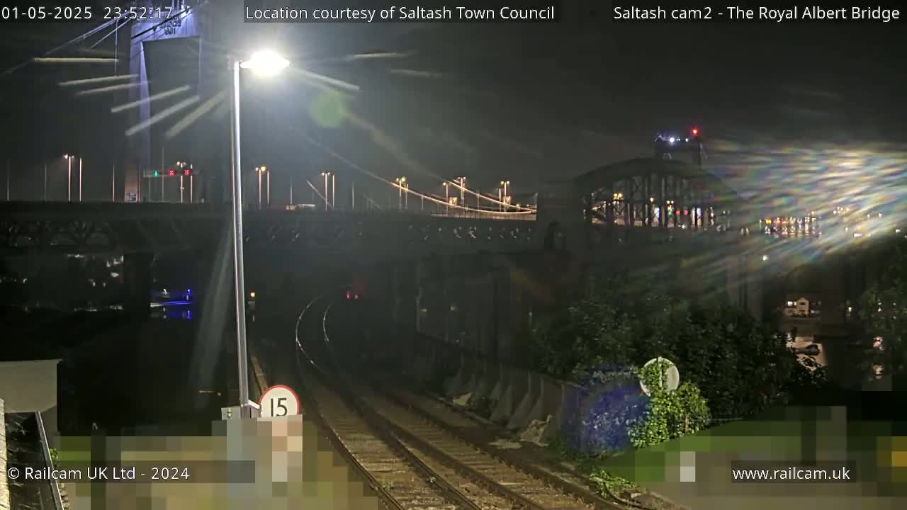A nighttime view of a bridge and train tracks, with a streetlight illuminating the scene.