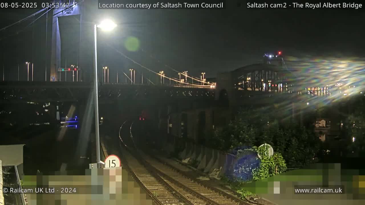 A nighttime view of railroad tracks leading toward a bridge and another structure beyond it, under clear skies.