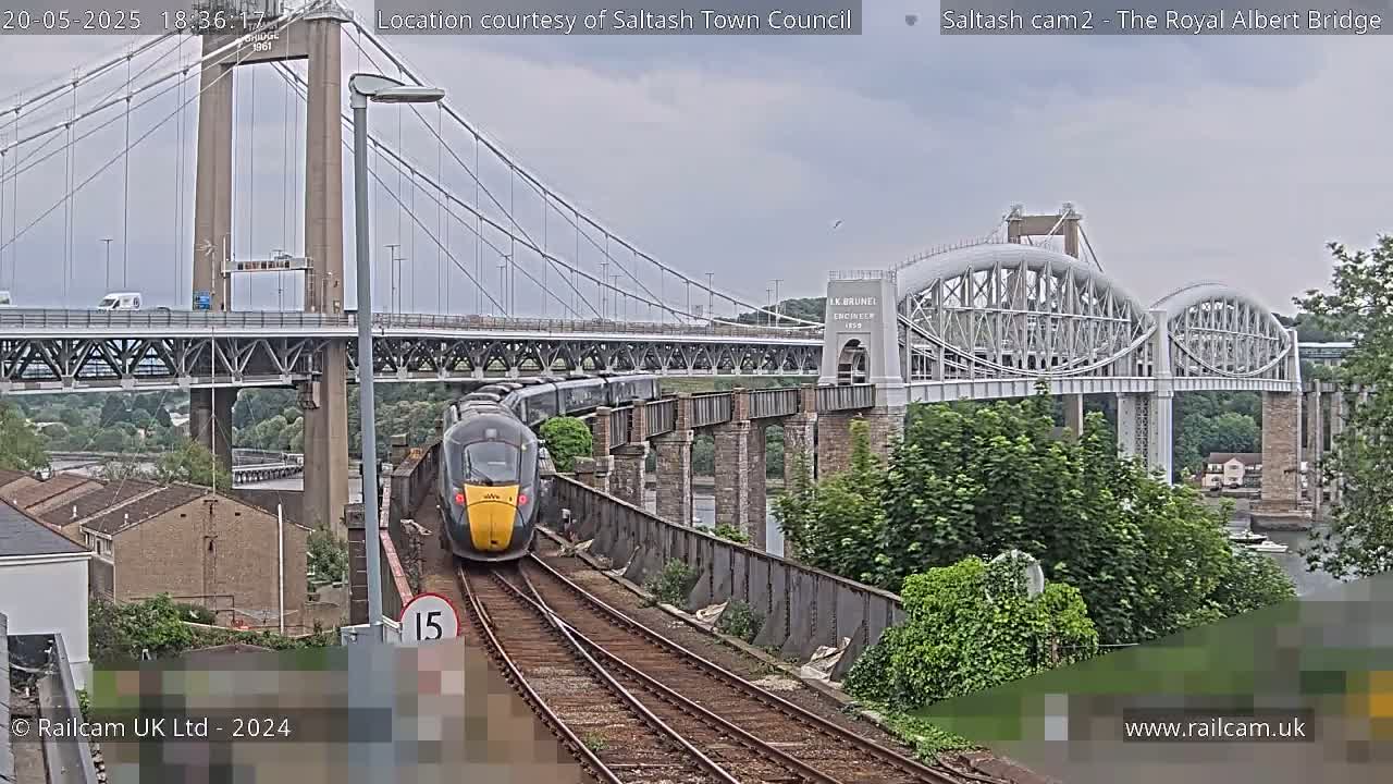 A train passes under a suspension bridge and an arched railway bridge on an overcast day.