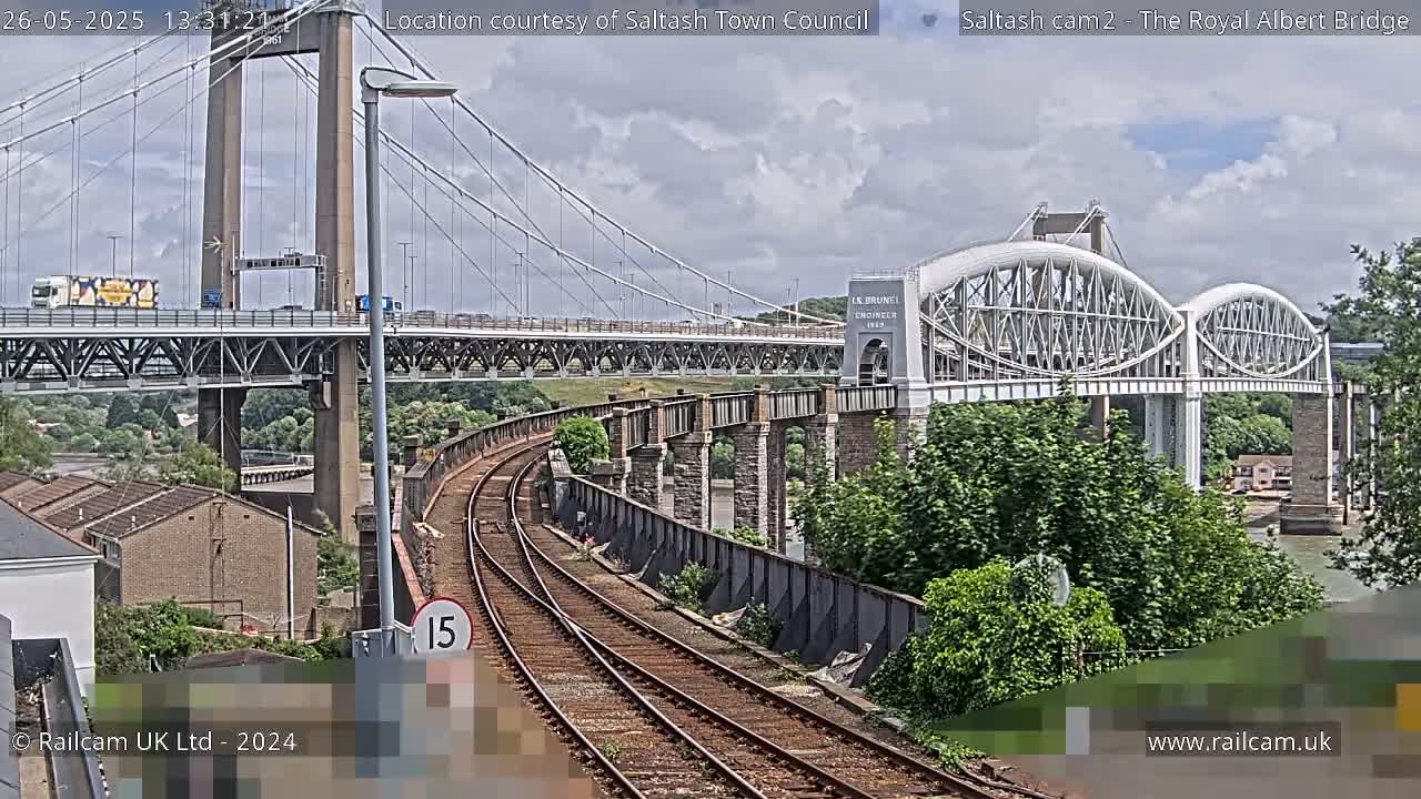 A view of a railway track leading to a double-decker bridge on a partly cloudy day.