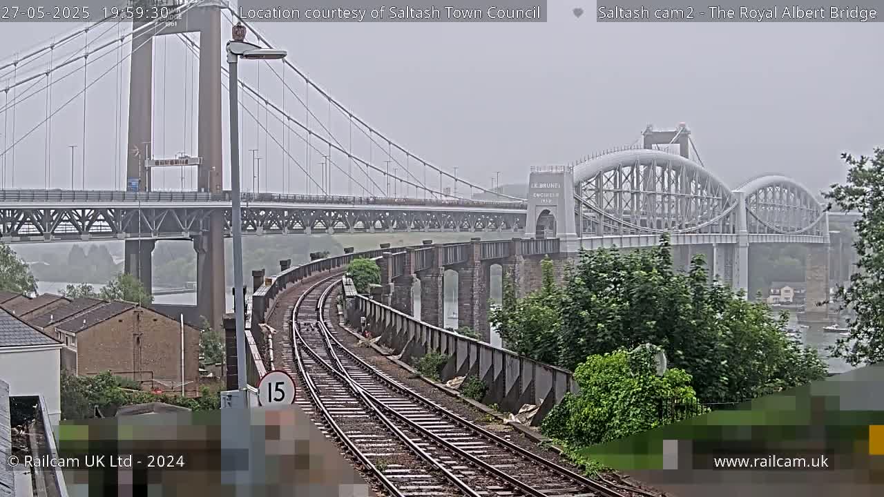 A railway line curves toward two bridges spanning a body of water under an overcast sky.
