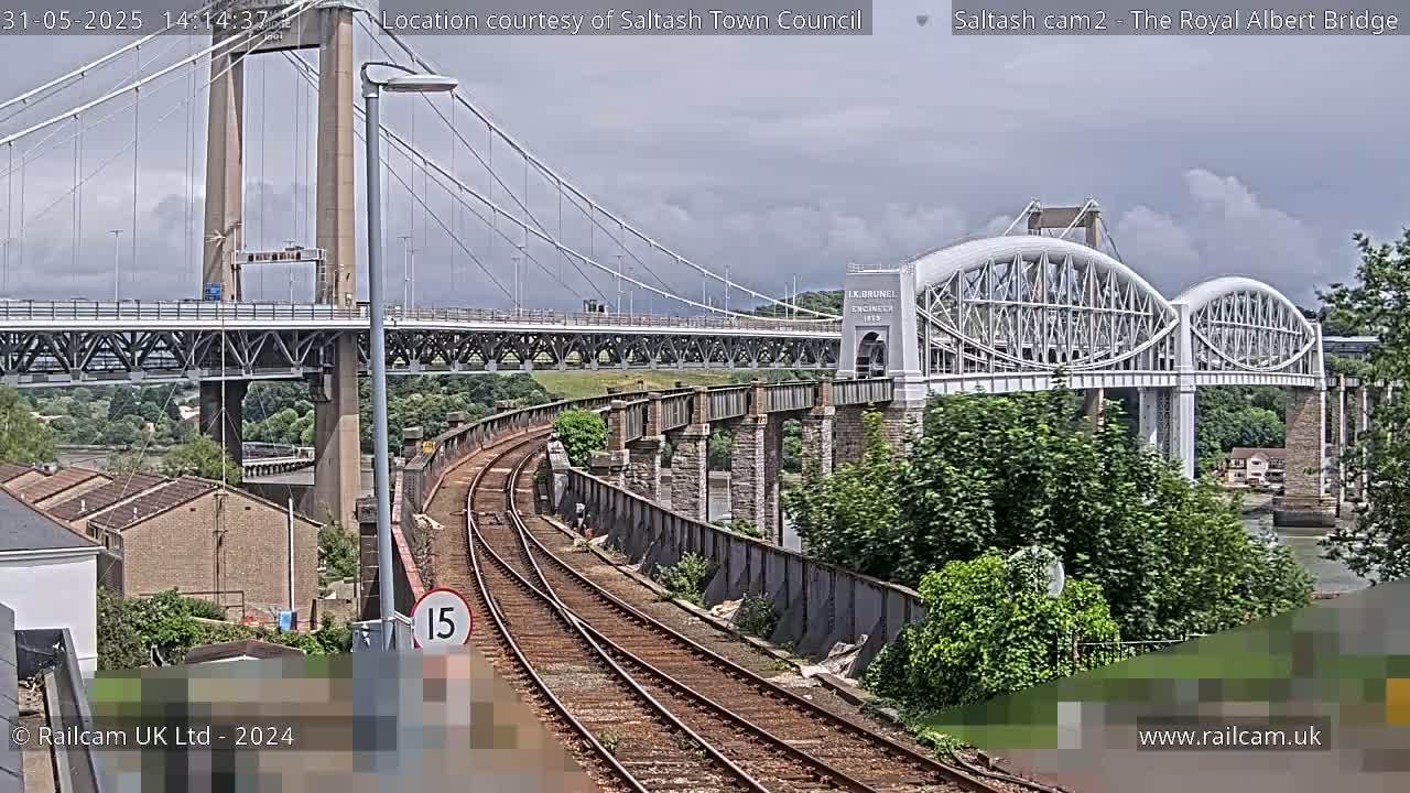 A view of a railway line leading to two bridges, one a suspension bridge and the other an arch bridge, under an overcast sky.