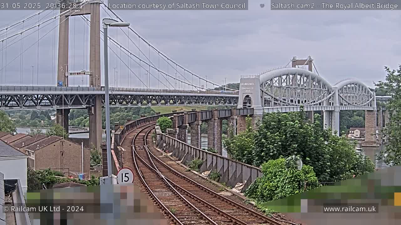 A view of railway tracks curving towards two bridges, one a suspension bridge and the other an arch bridge, under an overcast sky.