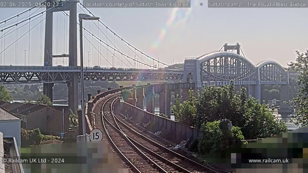 A sunny day shows two bridges spanning a body of water, with railroad tracks curving in the foreground.
