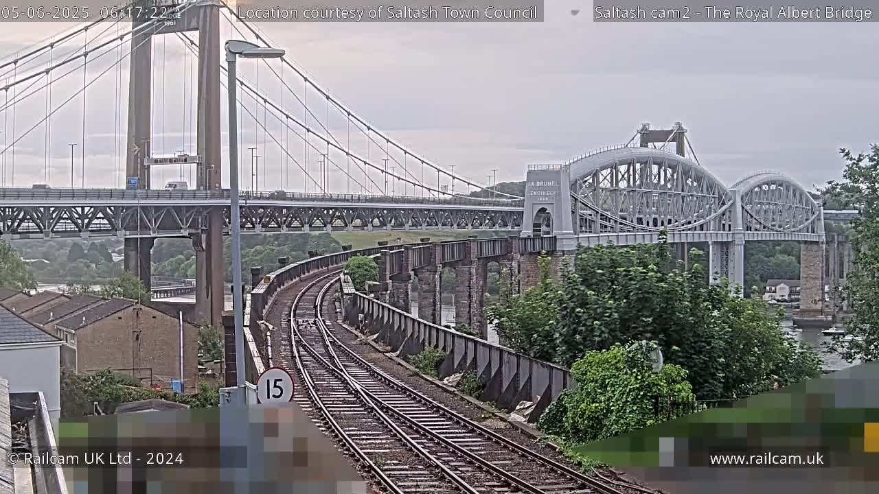 Train tracks curve toward two bridges, one a suspension bridge and the other an arch bridge, under an overcast sky.