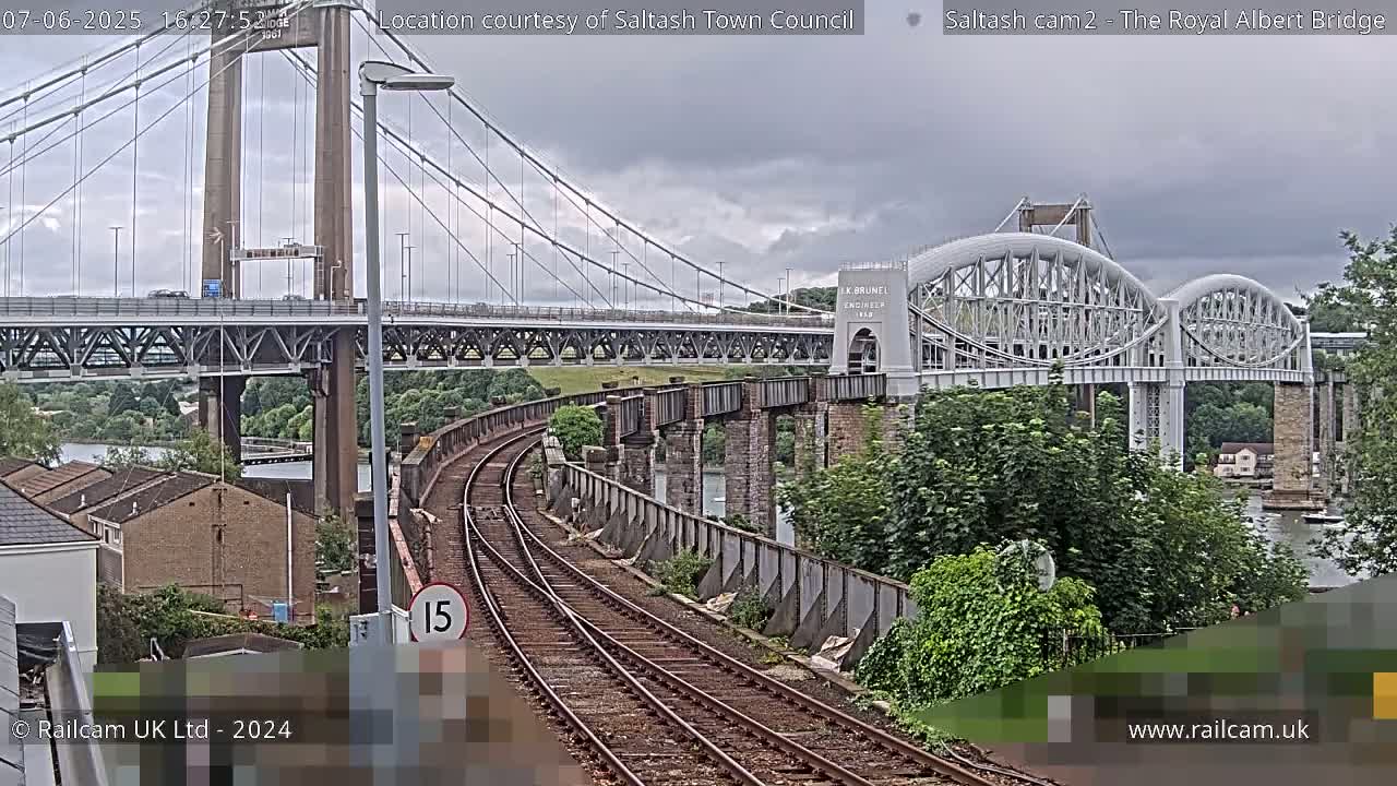 A view of railroad tracks curving towards two bridges spanning a body of water under an overcast sky.