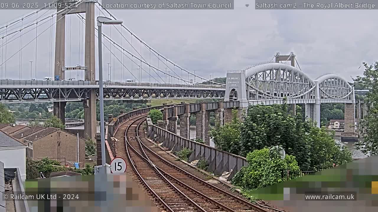 A view of a railway line leading to two bridges, one a suspension bridge and the other an arched bridge, on an overcast day.