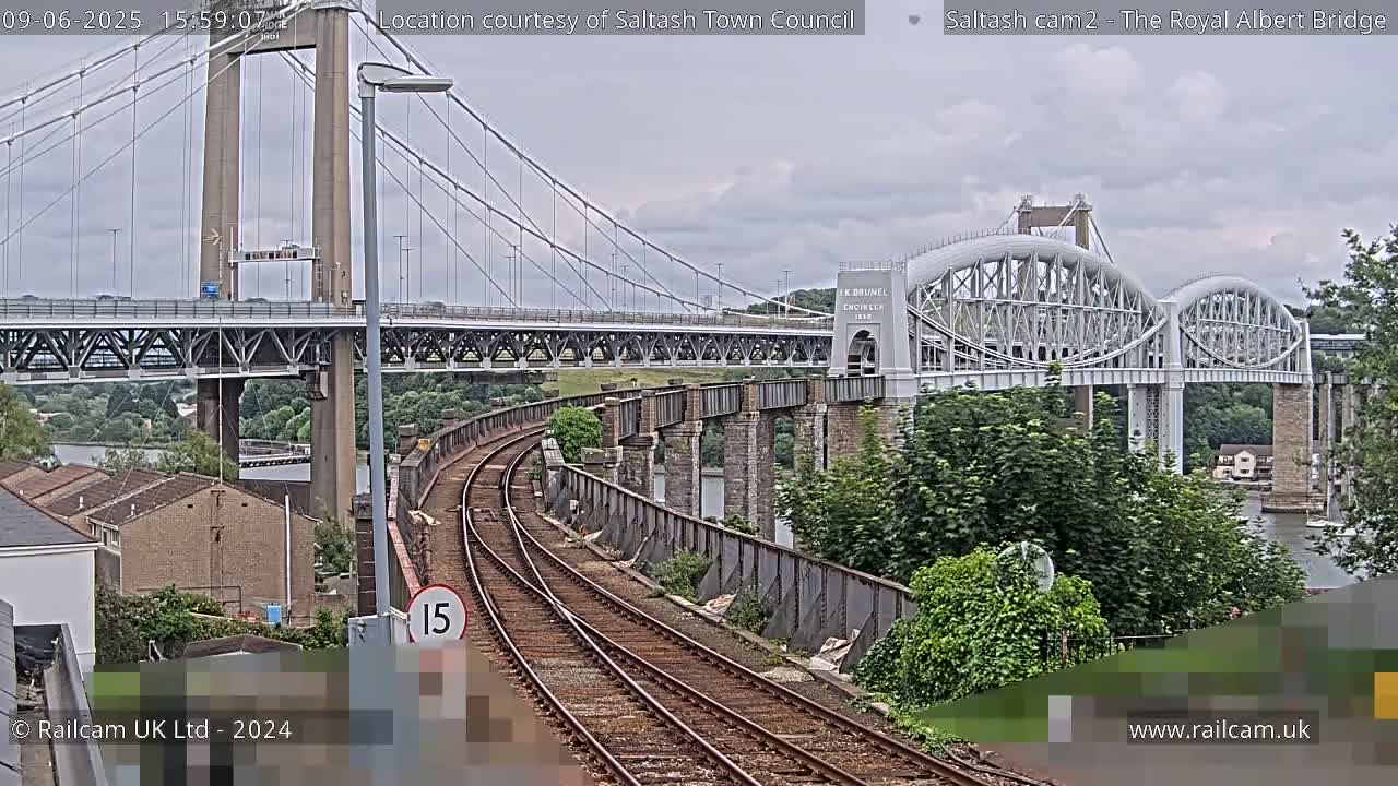 Train tracks curve toward two bridges, one a suspension bridge and the other an arch bridge, under a cloudy sky.