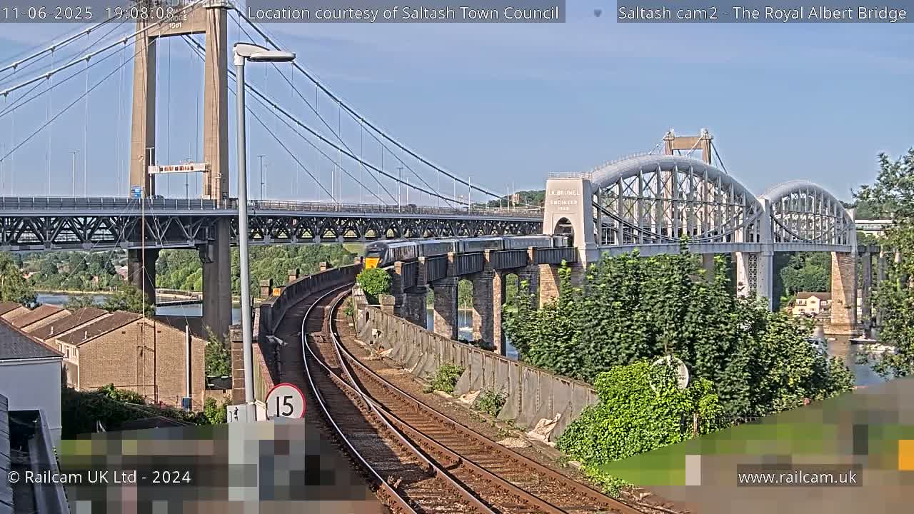 A train crosses a railway bridge under a suspension bridge on a sunny day.
