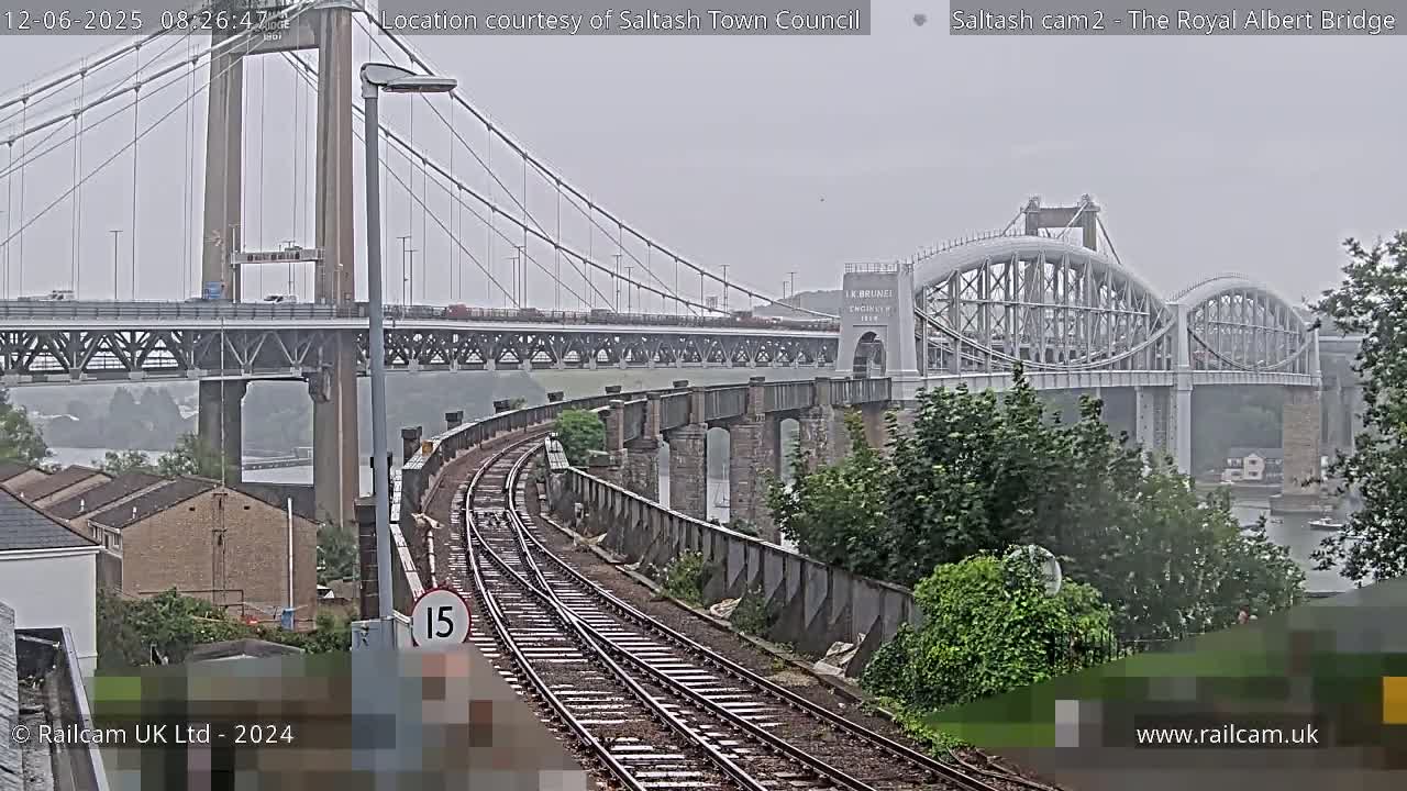 A view of railroad tracks curving toward two bridges spanning a river under an overcast sky.