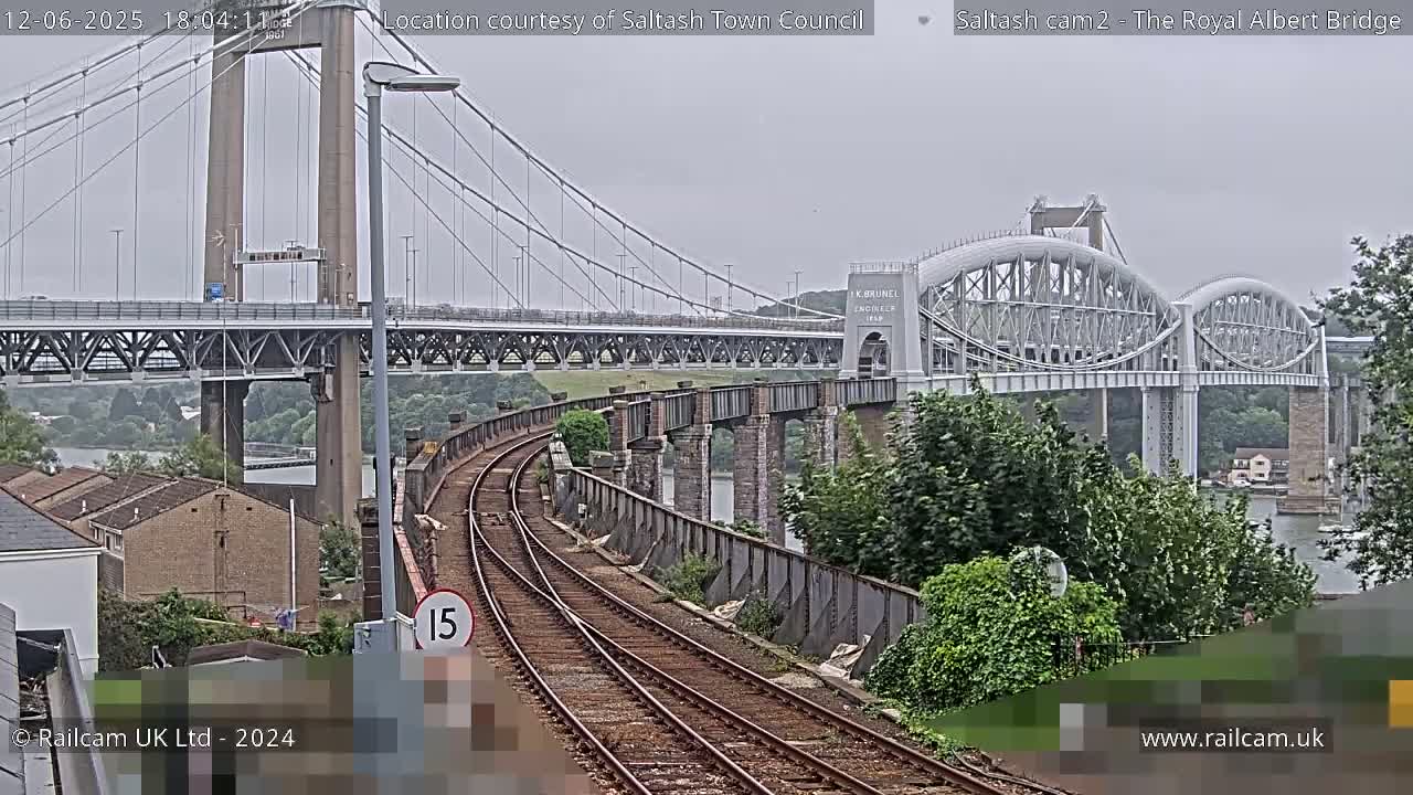 A view of railroad tracks leading to two bridges over a body of water under an overcast sky.
