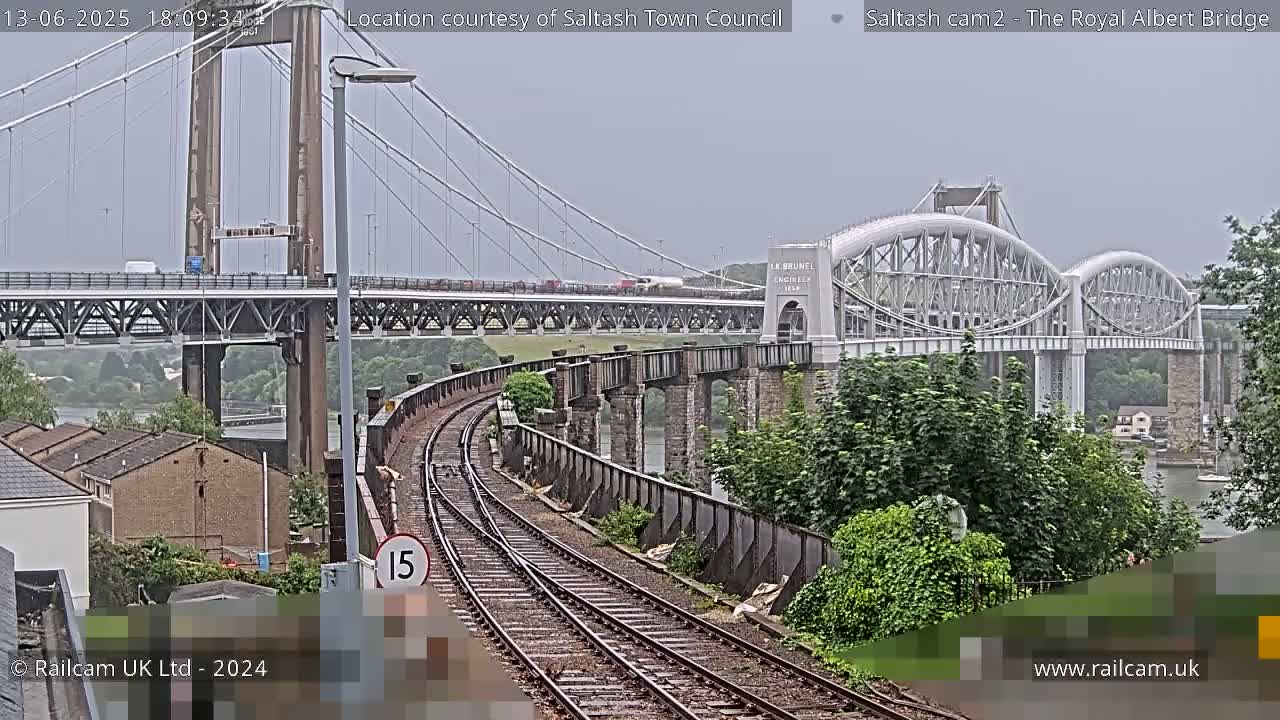 A railway track curves toward two bridges spanning a body of water under an overcast sky.