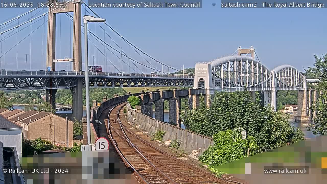 Two bridges span a river under a clear blue sky, with train tracks curving in the foreground.