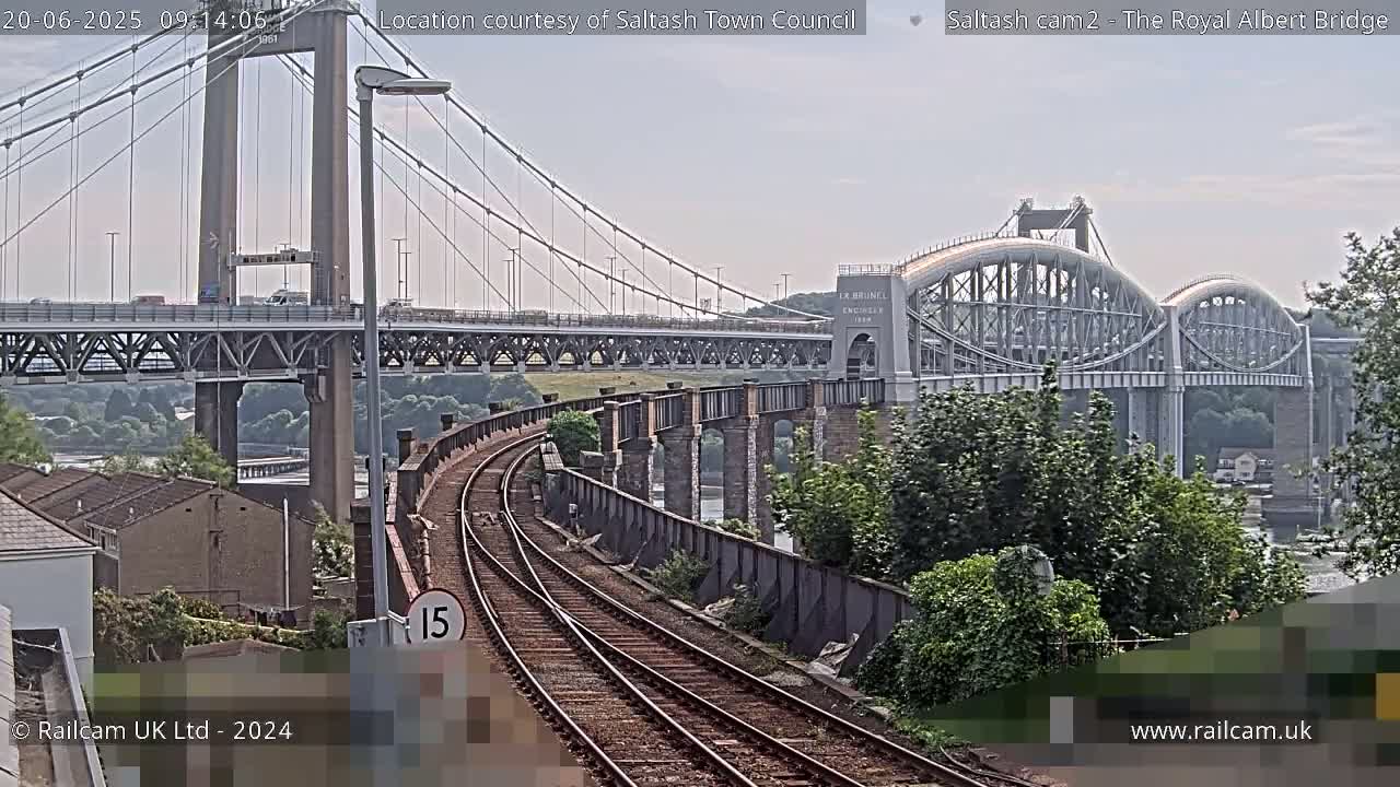 A view of a railway track curving towards two bridges on a partly cloudy day.