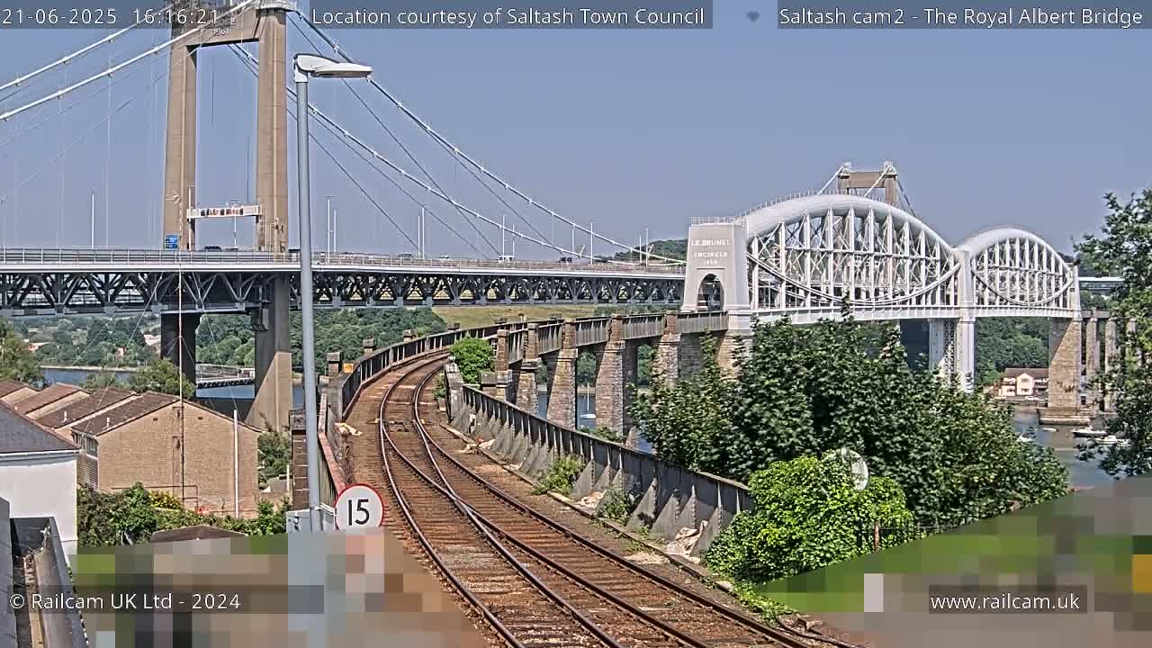 Train tracks curve toward two bridges on a sunny day, one a modern suspension bridge and the other a historic arch bridge.