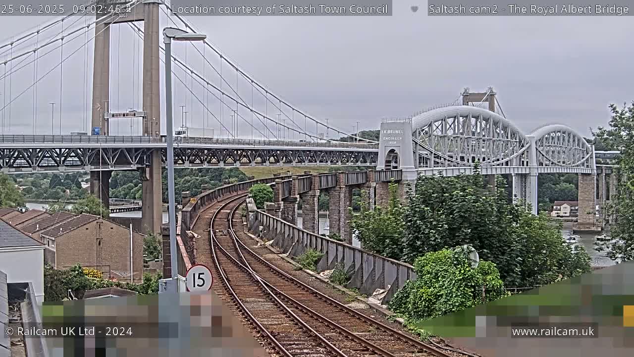 A view of train tracks curving toward two bridges spanning a waterway under an overcast sky.
