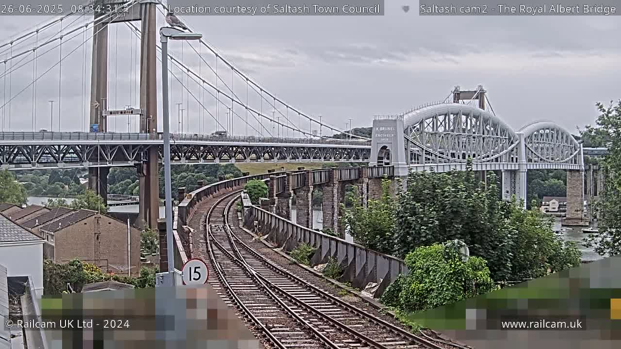 A railway line curves toward two bridges spanning a river under an overcast sky.