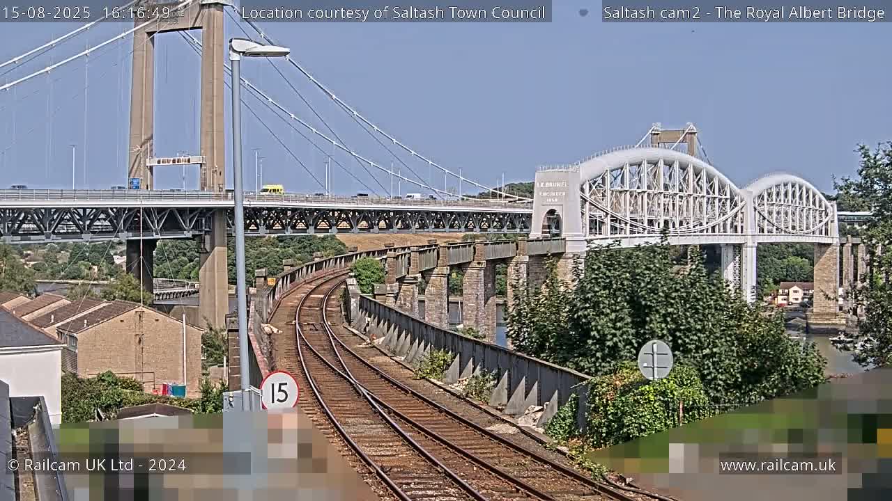 A train track curves towards two bridges, a suspension bridge and an arch bridge, under an overcast sky.
