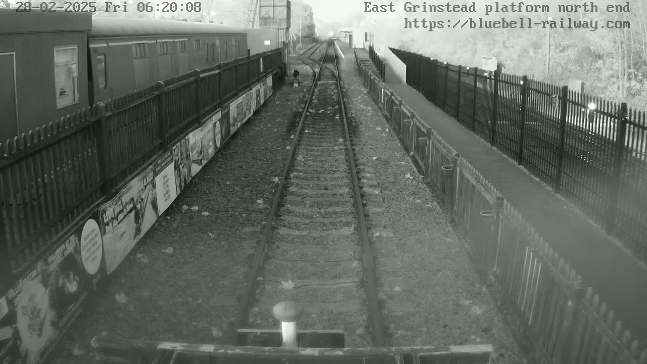 A railway platform with a train car alongside a fenced-in track on an overcast day.