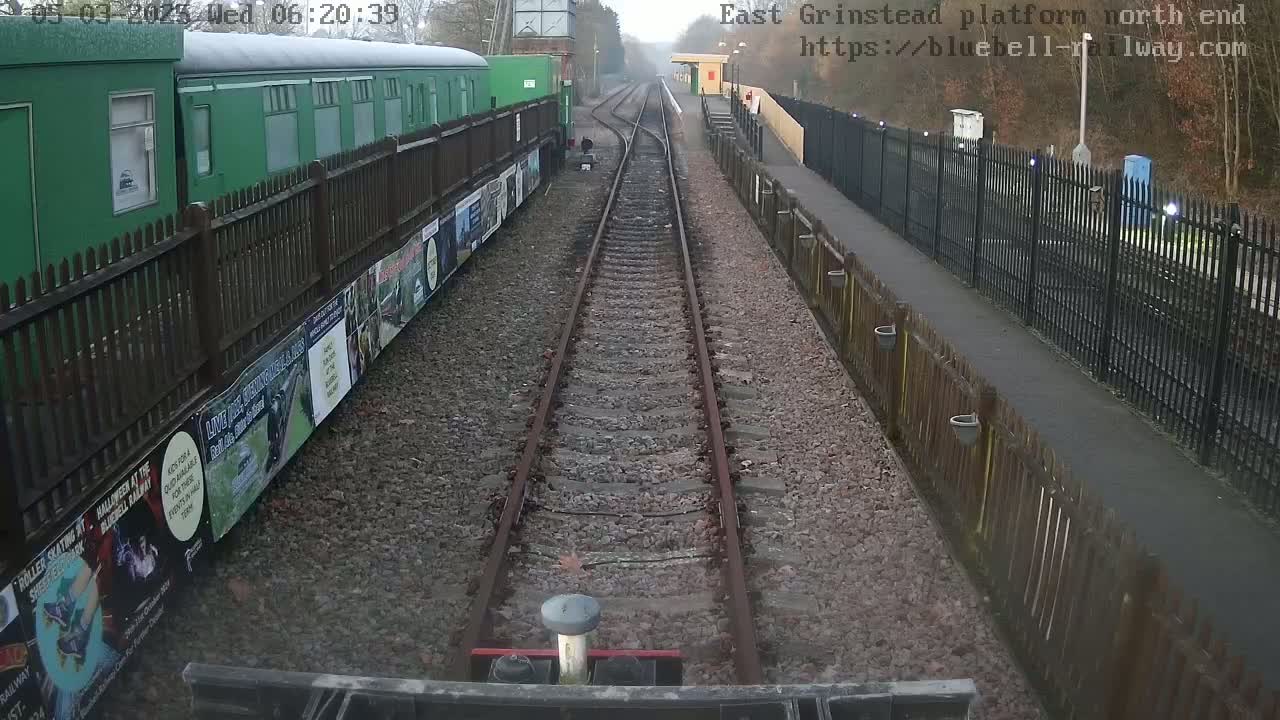 A view down a railway track on a foggy morning, with a green train car and wooden fences on either side.