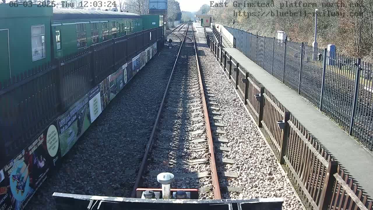 A view from a low vantage point down a train track on a sunny day, with a green train car and fences on either side.