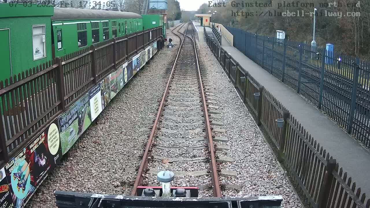 A view from a train's perspective down a railway track, passing a green railway carriage and a station platform on an overcast day.