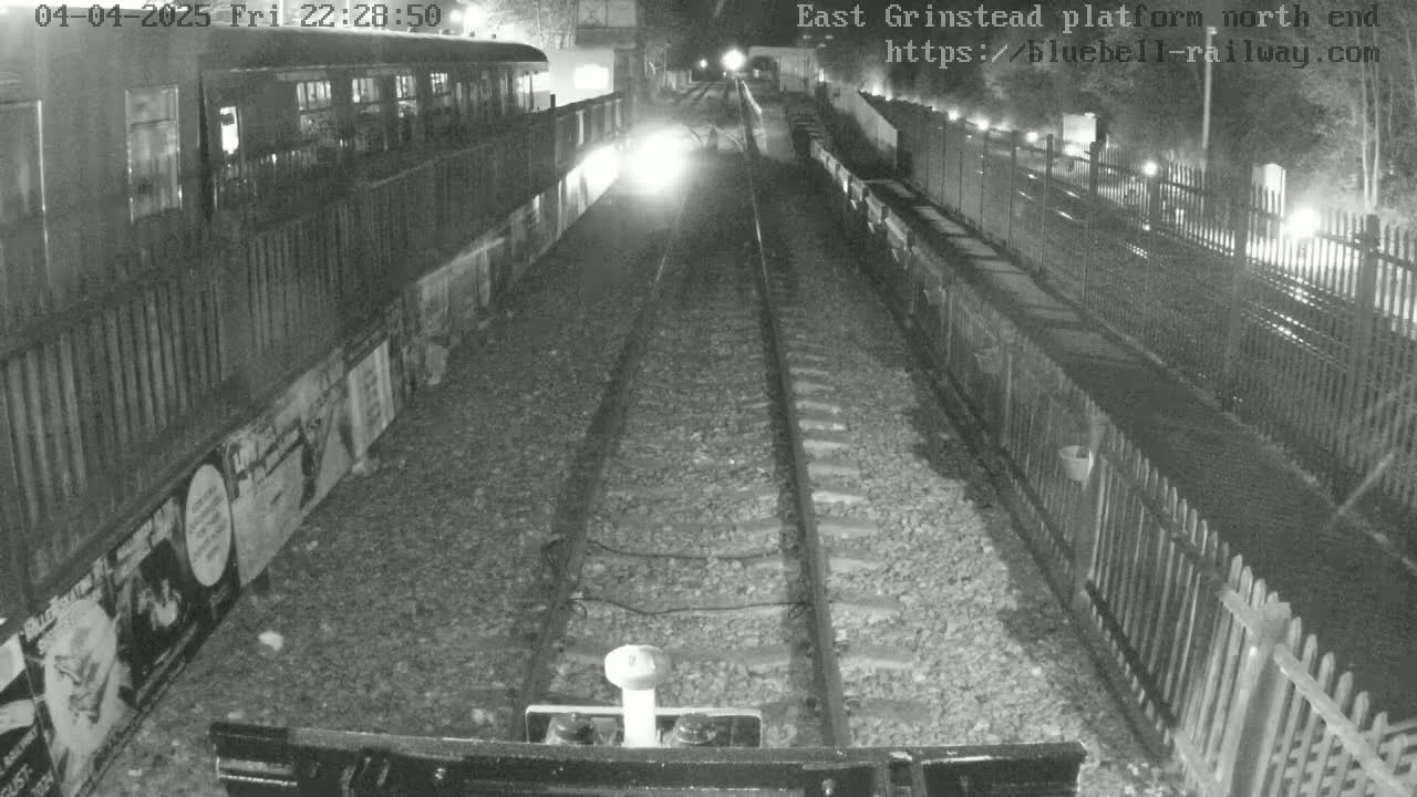 A nighttime view of train tracks at a station platform, with a train car visible to the side.