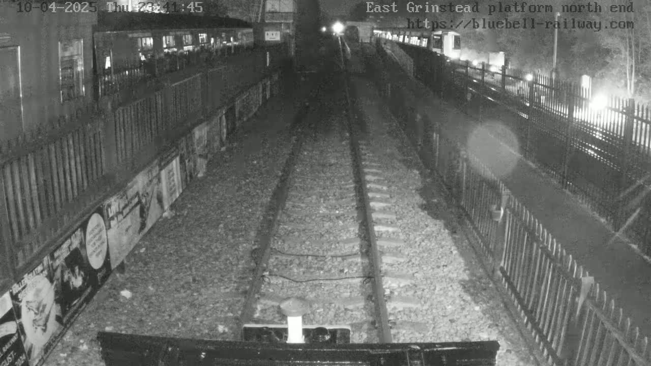 A nighttime view of train tracks at a station platform, with a train car visible to the left.