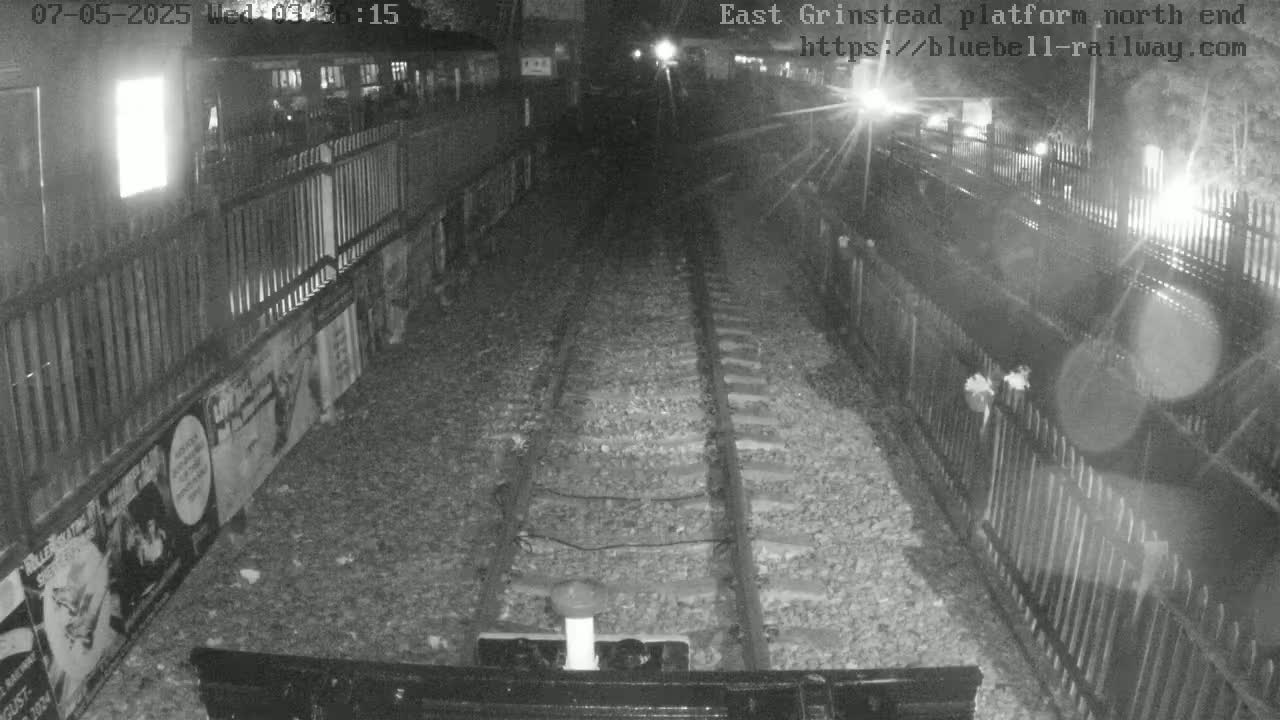 A nighttime view of train tracks between two fences, with posters on one side of the fence.