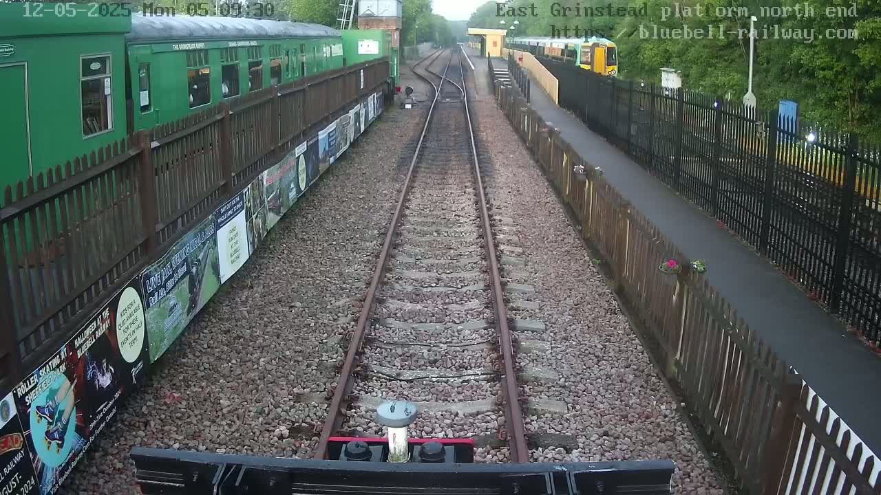 A view down a railway track on an overcast day, with green railway cars and fences on either side.