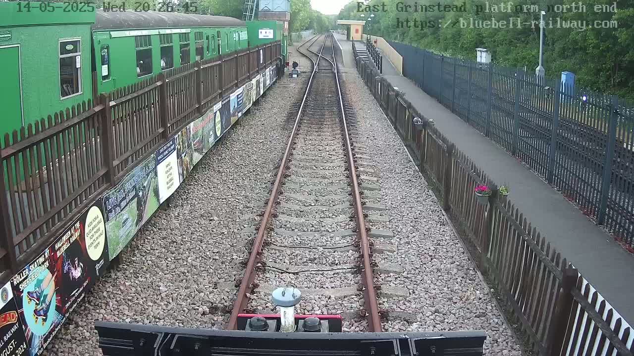 A view down a railway track, bordered by fences and a green train car, on an overcast day.