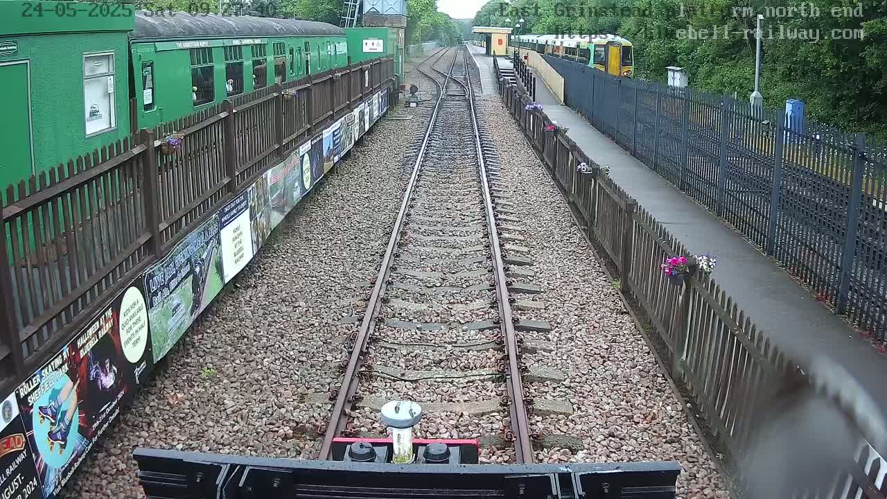 A view down a railway track on a cloudy day, with a green train car to the left and a yellow train in the distance.