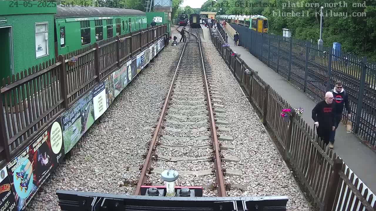 A view from a train on a railway track, showing railway cars and people, on a partly sunny day.