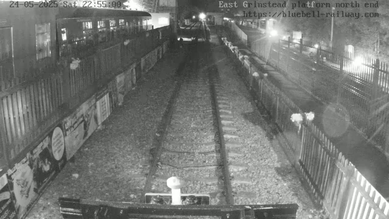 A nighttime, low-light view down a railway track between two platforms with fences and posters on the sides.