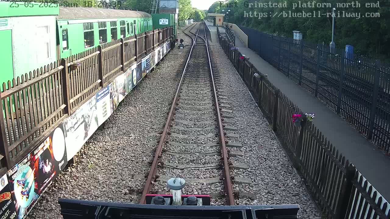 A railway track stretches towards a green train parked at a station platform on a sunny day.