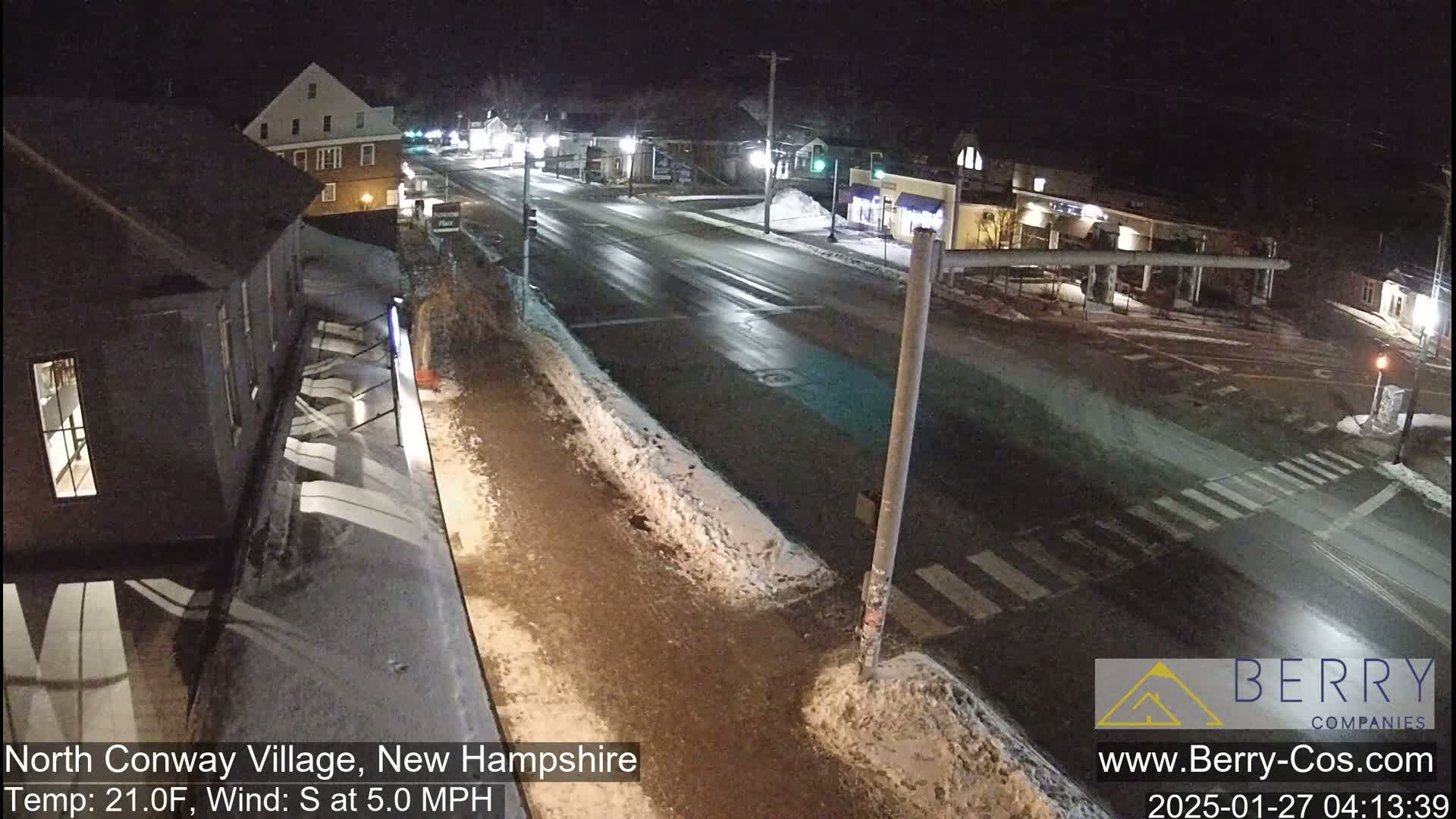 A nighttime street scene shows a mostly empty roadway with some snow on the sides, under partly cloudy skies.